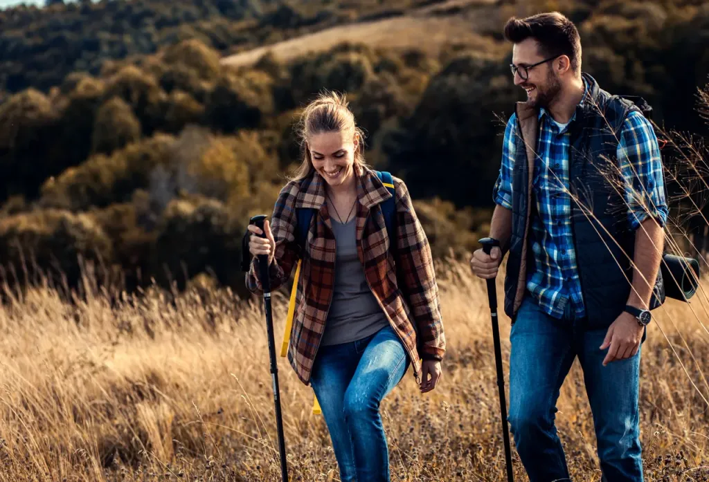 Woman and man hiking with trekking poles through a golden meadow