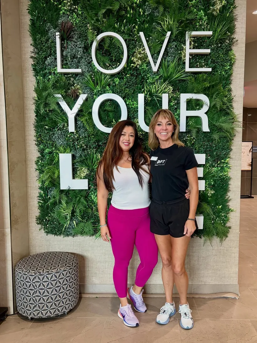 Robyn with a participant at a community wellness event, in front of a Love Your Life wall