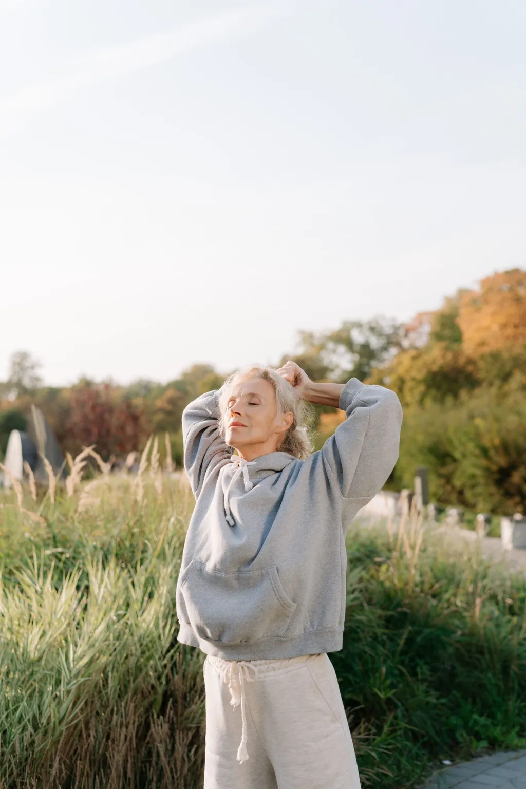 Mature woman stretching her arms overhead outdoors in tall grass