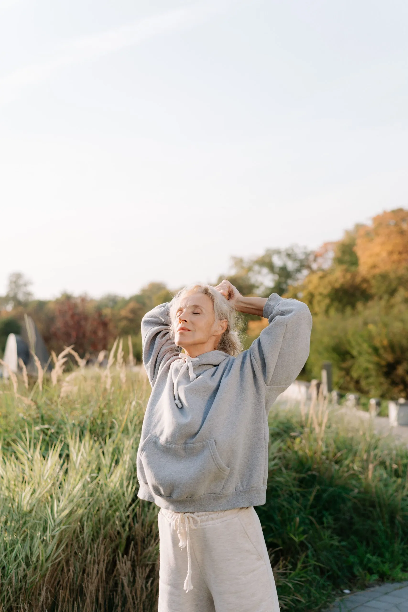 Mature woman stretching her arms overhead outdoors in tall grass