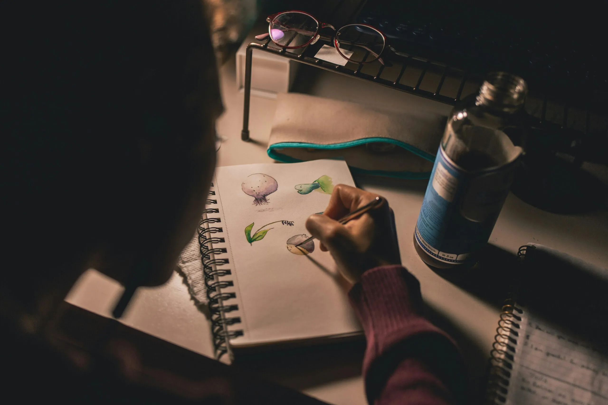 Person sketching in a notebook at a dimly lit desk