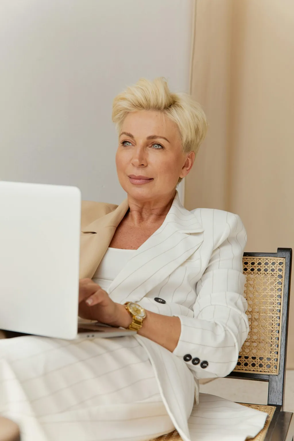 Woman with short blond hair in a white blazer working on a laptop
