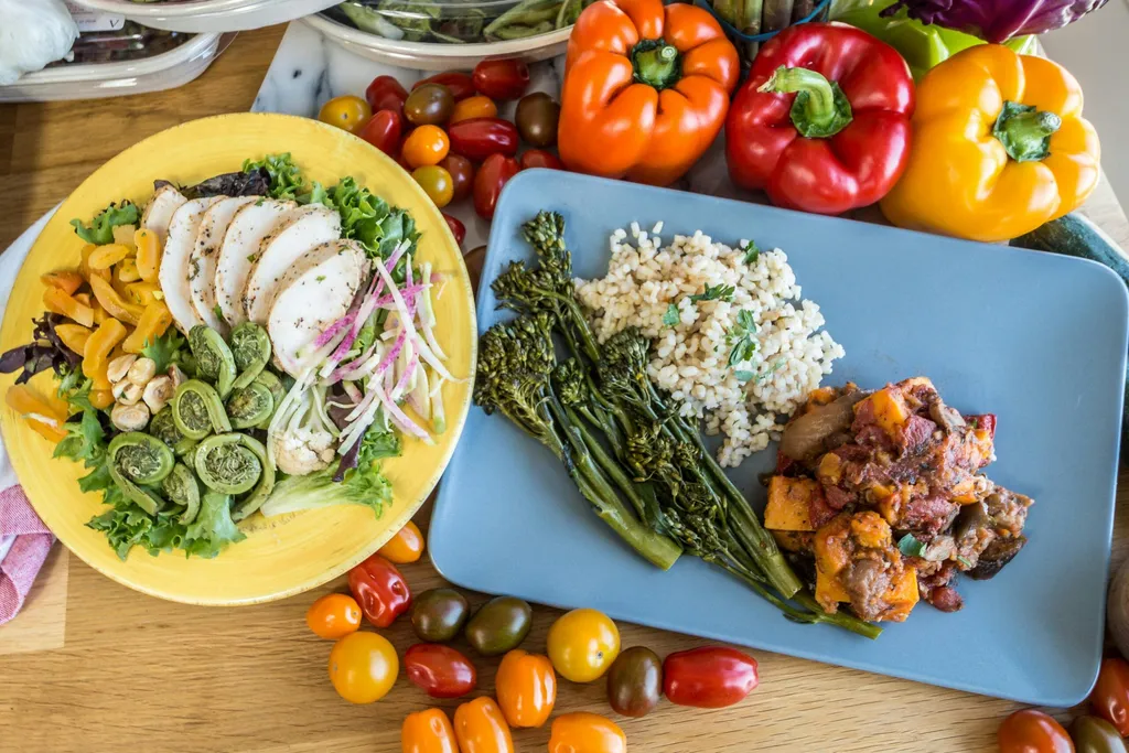 Plates of chicken salad, green beans, rice and vegetables with fresh peppers and tomatoes